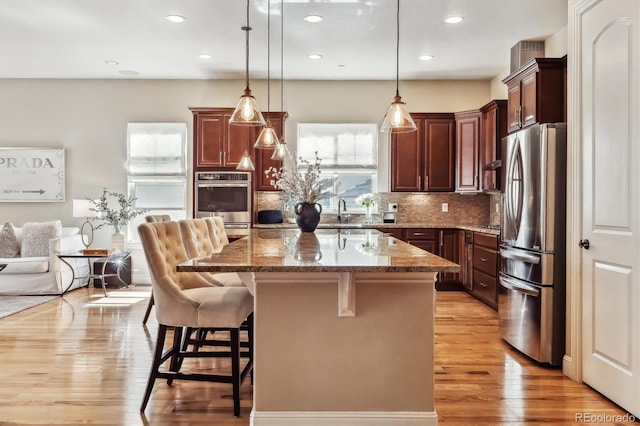 kitchen with a kitchen breakfast bar, dark stone countertops, freestanding refrigerator, light wood-type flooring, and backsplash