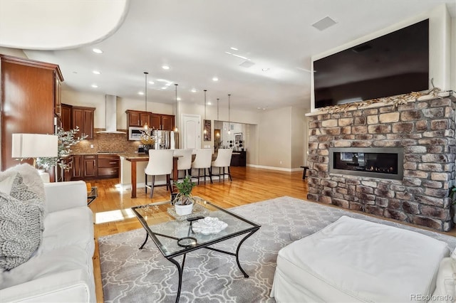 living room with light wood-type flooring, a brick fireplace, baseboards, and recessed lighting