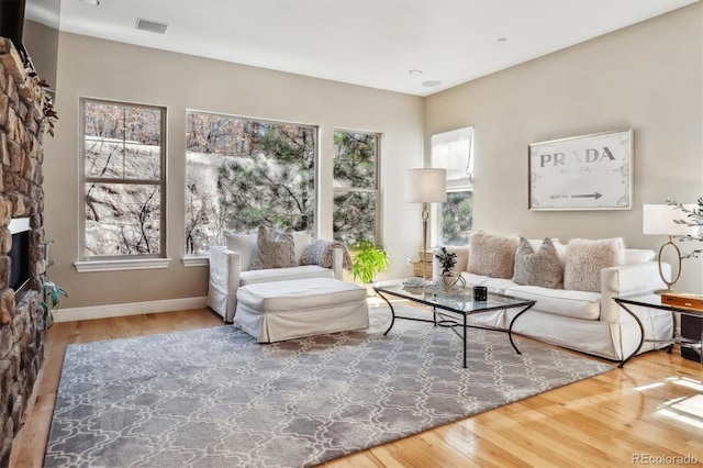 living area featuring visible vents, a stone fireplace, baseboards, and hardwood / wood-style flooring