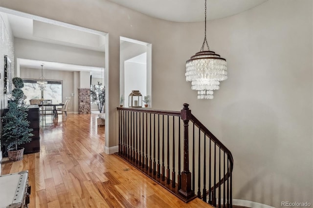 hall featuring wood-type flooring, baseboards, an upstairs landing, and an inviting chandelier