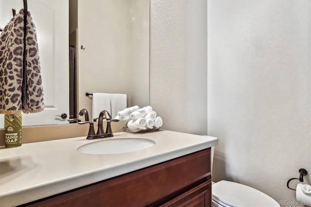 bathroom featuring a textured wall, vanity, and toilet