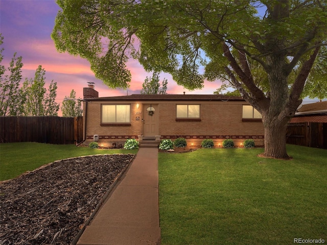 ranch-style house featuring brick siding, a chimney, a front yard, and fence