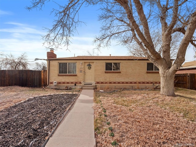 ranch-style home with a chimney, fence, and brick siding