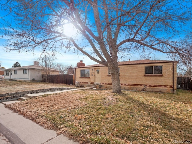 single story home with entry steps, brick siding, a chimney, fence, and a front yard