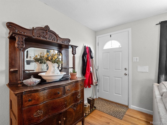 foyer entrance featuring a textured ceiling, light wood-type flooring, and baseboards