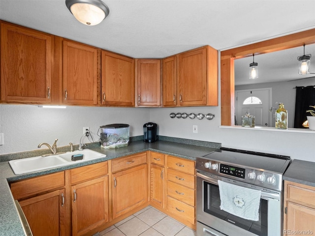 kitchen with brown cabinets, light tile patterned floors, dark countertops, electric range, and a sink