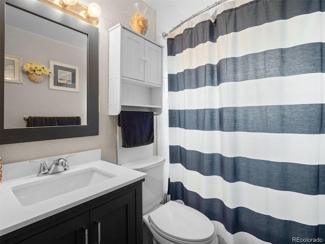 bathroom with a shower with curtain, a textured wall, vanity, and toilet