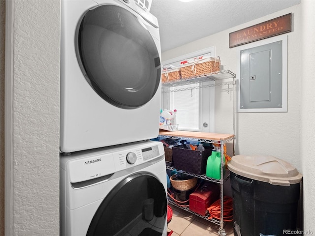 laundry room featuring stacked washer and dryer, laundry area, electric panel, tile patterned floors, and a textured ceiling