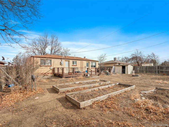 back of house featuring an outbuilding, a deck, a storage shed, fence, and a vegetable garden