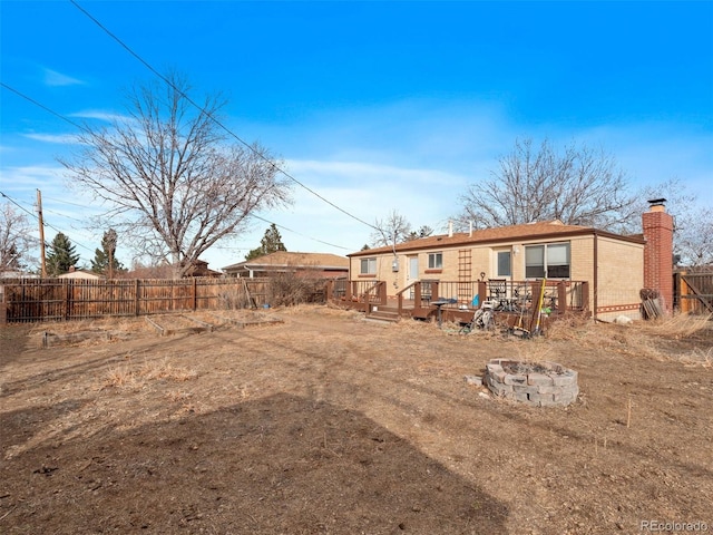 back of property with brick siding, a chimney, a deck, a fenced backyard, and a fire pit