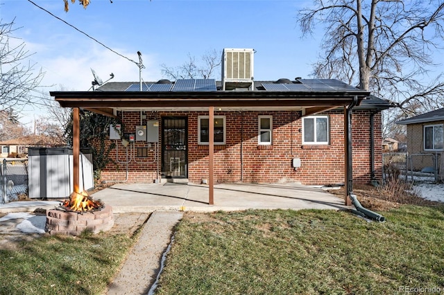 rear view of house with a patio, a yard, solar panels, central AC unit, and a fire pit