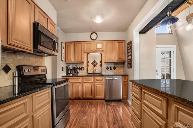 kitchen with dark stone counters, appliances with stainless steel finishes, dark wood-style flooring, a sink, and backsplash