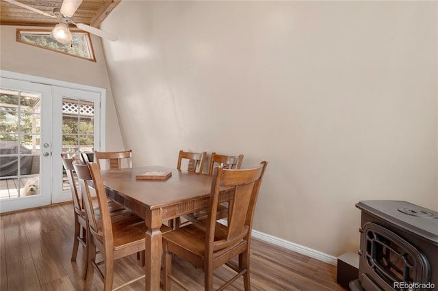 dining room featuring baseboards, french doors, a high ceiling, a wood stove, and wood finished floors