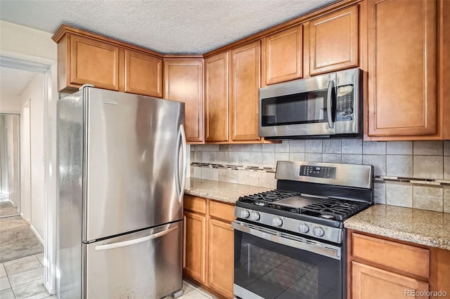 kitchen with light stone countertops, tasteful backsplash, a textured ceiling, light tile patterned floors, and appliances with stainless steel finishes