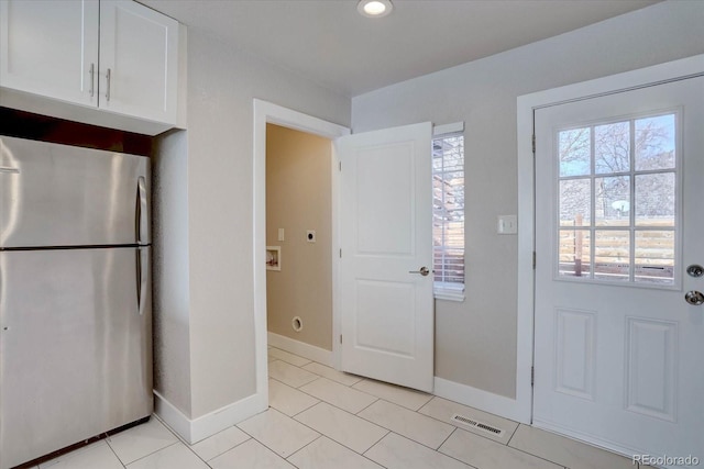 kitchen with stainless steel refrigerator, white cabinetry, and light tile patterned flooring