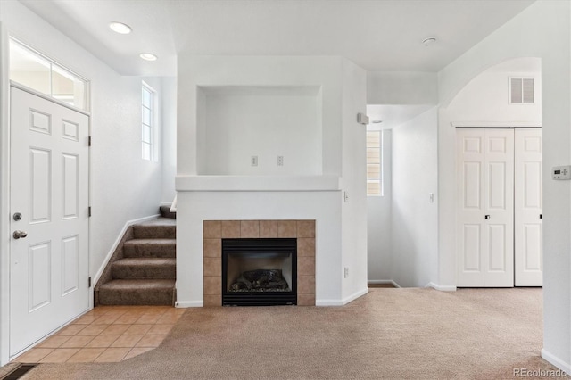 unfurnished living room with a tiled fireplace, a healthy amount of sunlight, and light colored carpet