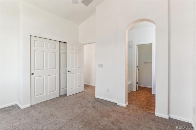 unfurnished bedroom featuring vaulted ceiling, a closet, ensuite bath, light colored carpet, and ceiling fan