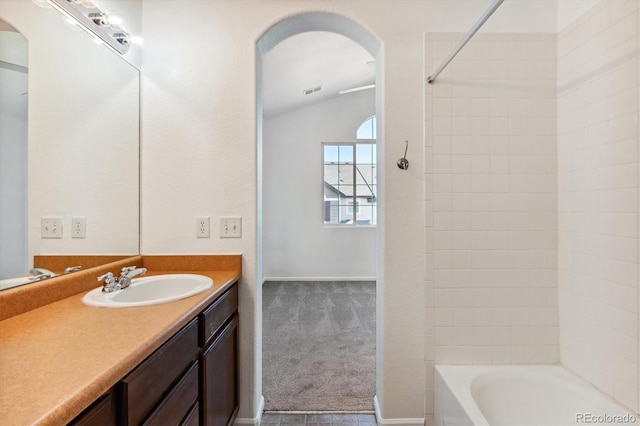 bathroom featuring lofted ceiling, tiled shower / bath, and vanity