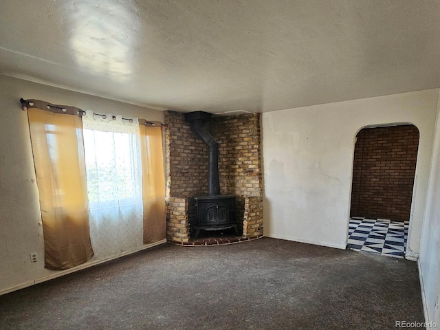 unfurnished living room with carpet floors, a textured ceiling, and a wood stove