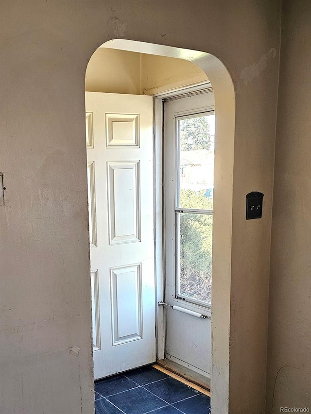 doorway to outside with arched walkways and dark tile patterned flooring