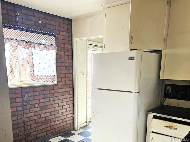 kitchen featuring tile patterned floors, brick wall, and freestanding refrigerator