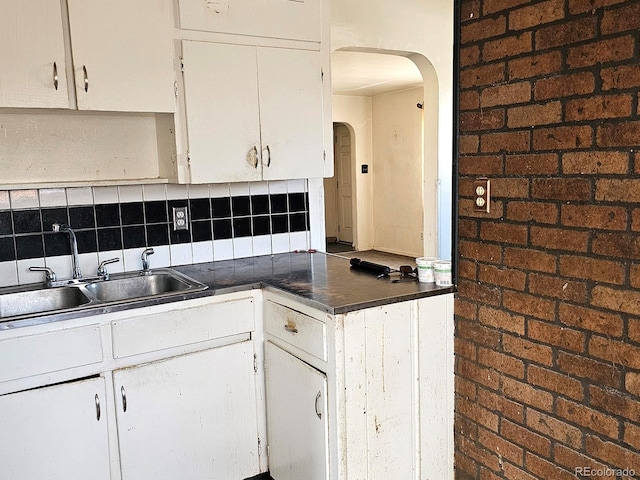 kitchen featuring white cabinetry, arched walkways, backsplash, and a sink