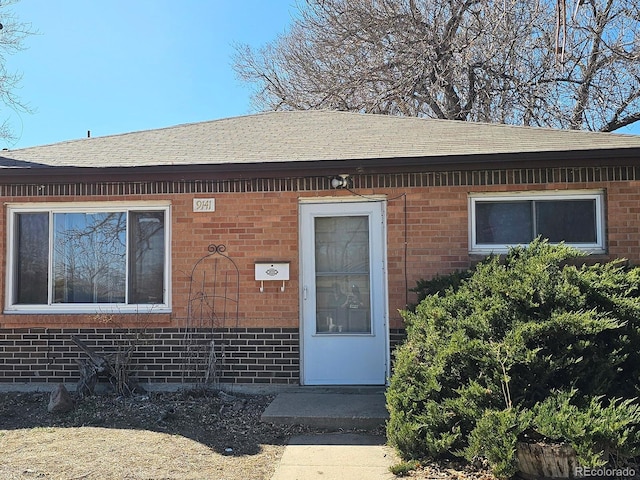 entrance to property featuring brick siding and roof with shingles