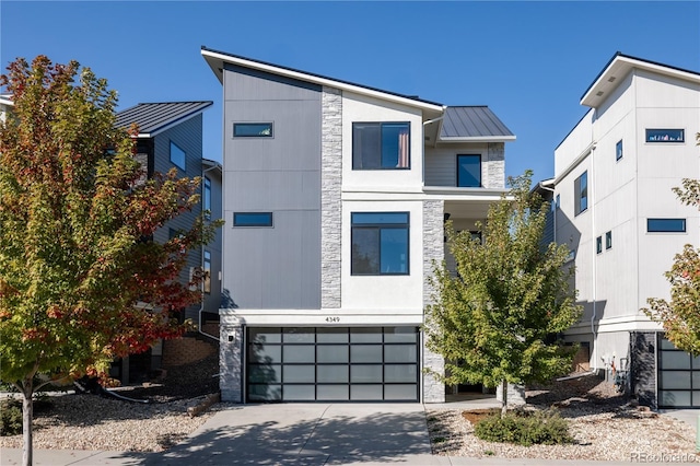 contemporary house featuring concrete driveway, stone siding, metal roof, an attached garage, and a standing seam roof