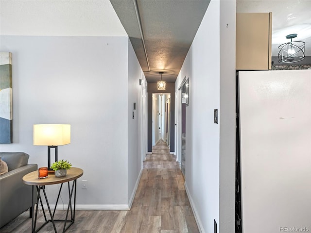 hall with a textured ceiling, baseboards, and wood finished floors