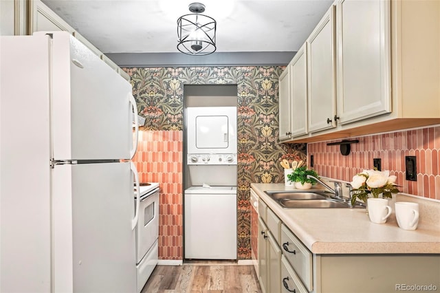 kitchen with wallpapered walls, light countertops, stacked washer and clothes dryer, white appliances, and a sink