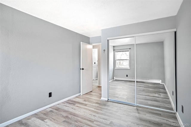 unfurnished bedroom featuring a closet, baseboard heating, baseboards, and wood finished floors