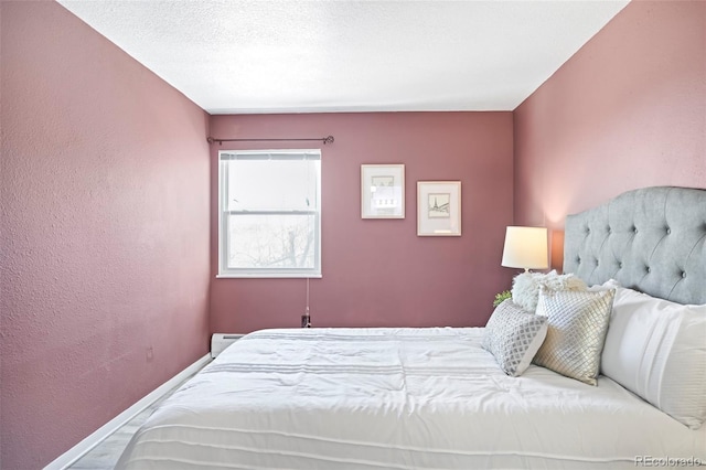 bedroom featuring a baseboard radiator, baseboards, a textured ceiling, and a textured wall