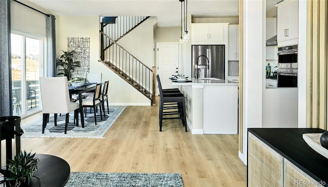 kitchen featuring appliances with stainless steel finishes, decorative light fixtures, light wood-type flooring, a kitchen bar, and white cabinetry