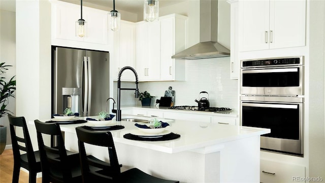 kitchen with a breakfast bar, white cabinets, wall chimney range hood, appliances with stainless steel finishes, and tasteful backsplash