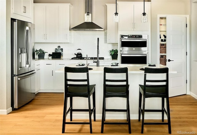 kitchen with stainless steel appliances, light countertops, light wood-style flooring, and wall chimney range hood