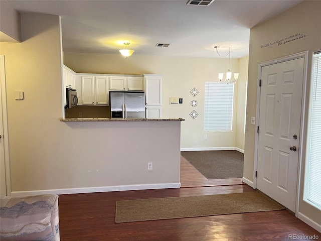 kitchen with a chandelier, dark wood-type flooring, a peninsula, stainless steel appliances, and white cabinetry