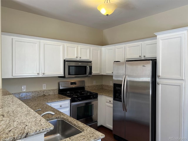 kitchen with light stone counters, white cabinetry, stainless steel appliances, and a sink