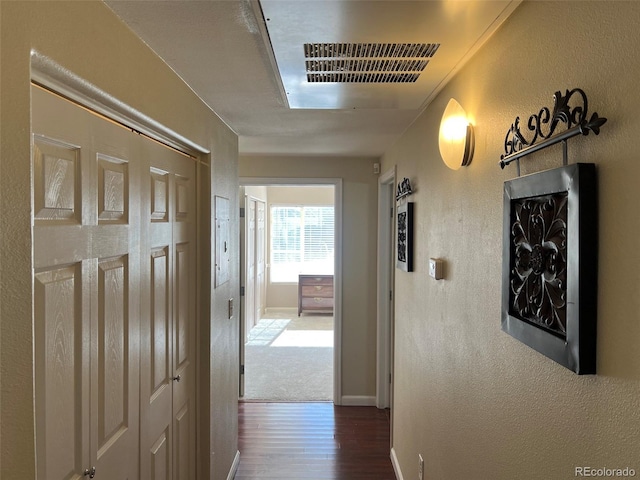 hall featuring dark wood-style floors, a textured wall, visible vents, and baseboards