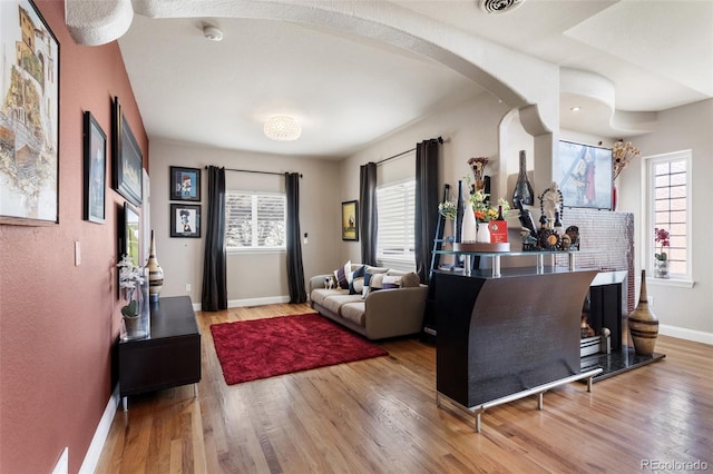 living room with light wood-type flooring, baseboards, and arched walkways