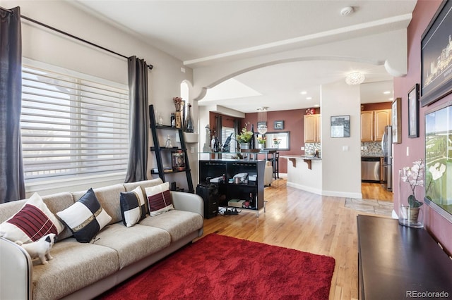 living room with light wood finished floors, baseboards, and arched walkways