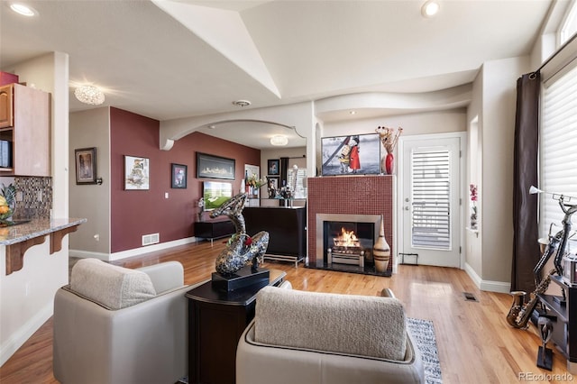 living room with arched walkways, a fireplace, visible vents, light wood-type flooring, and baseboards