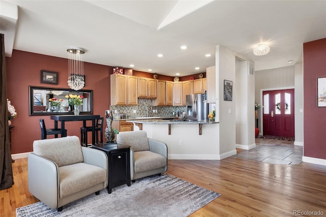 kitchen with a breakfast bar area, backsplash, light wood-style floors, stainless steel fridge, and a peninsula