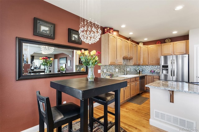 kitchen with stainless steel appliances, hanging light fixtures, light stone counters, and a sink