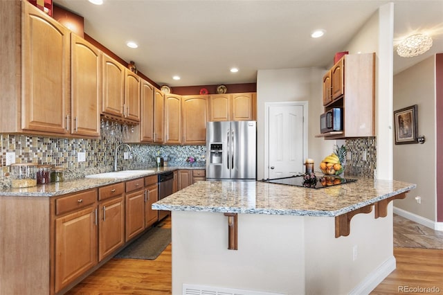 kitchen with light stone counters, a breakfast bar area, a sink, a peninsula, and black appliances