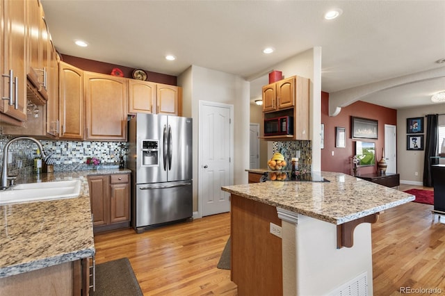 kitchen featuring arched walkways, light wood-style flooring, a sink, light stone countertops, and black appliances