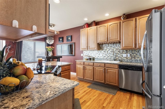 kitchen with light wood finished floors, appliances with stainless steel finishes, a sink, light stone countertops, and backsplash