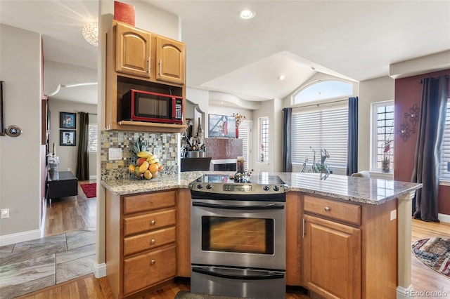 kitchen with a peninsula, light stone counters, stainless steel range with electric stovetop, and tasteful backsplash