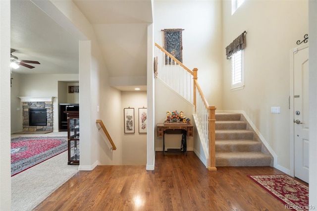 entrance foyer with stairs, a stone fireplace, a high ceiling, and wood finished floors