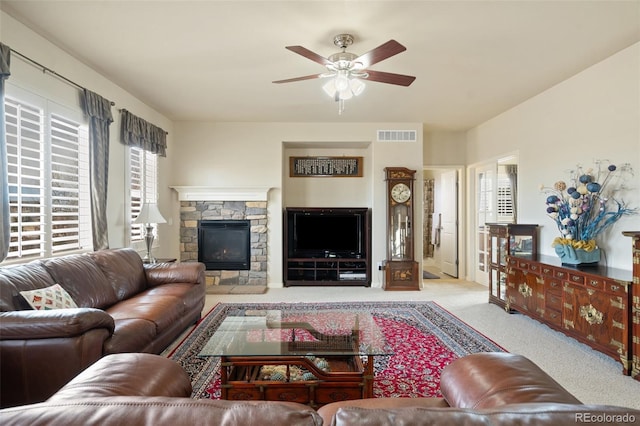 carpeted living room with a ceiling fan, visible vents, and a stone fireplace