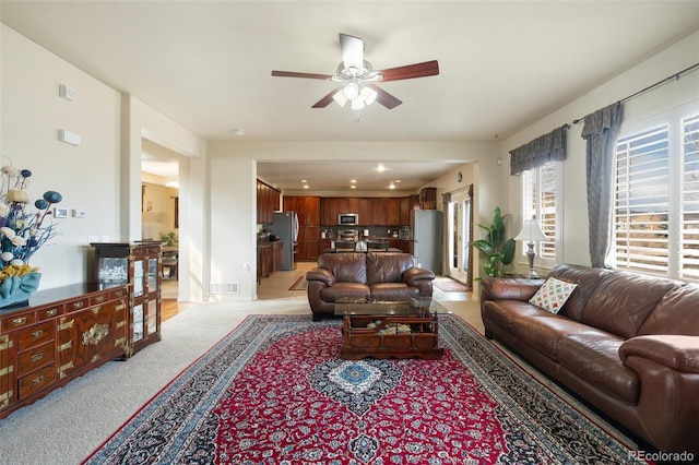 living room featuring a ceiling fan, visible vents, and light colored carpet